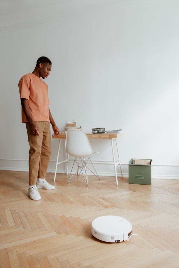 stats-img Man in casual attire looking at robot vacuum in a modern home office setting.