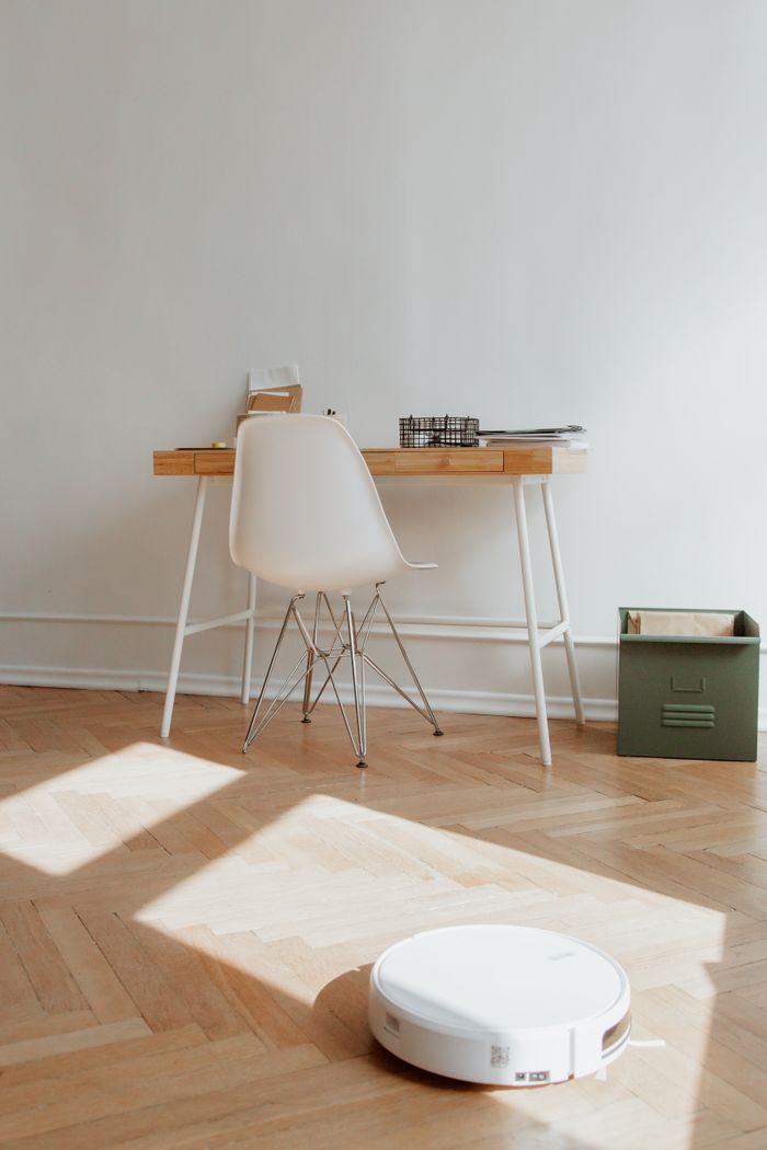 why-choose-us A modern home office setup featuring a desk and robotic vacuum on a wooden floor, highlighting minimalism.