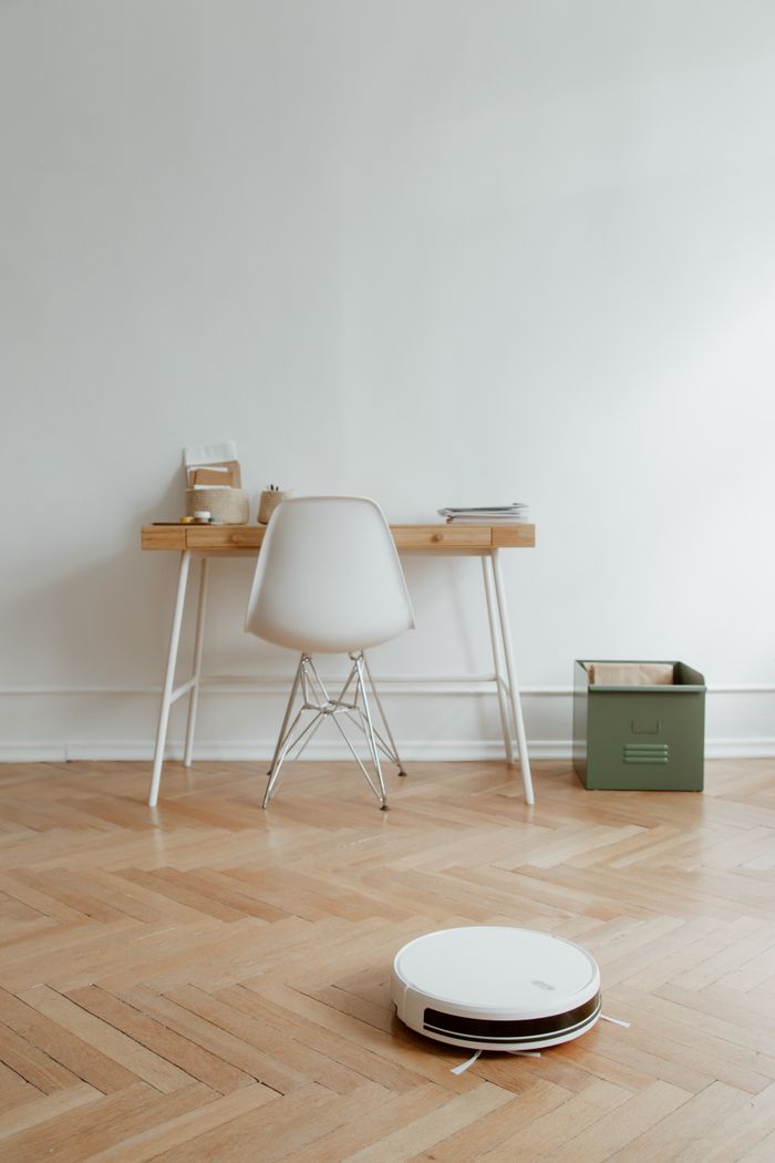 portfolio-01 A sleek home office setup with a robot vacuum cleaning the wooden floor, emphasizing minimalism.